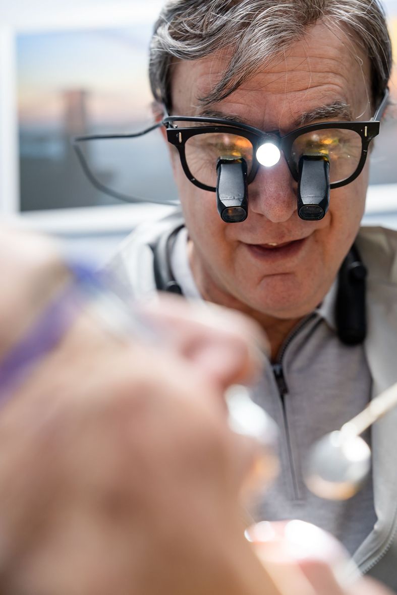 Doctor wearing binocular loupes examines a patient in a bright clinic.
