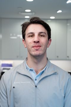 Man standing in a bright office, wearing a light blue jacket and looking at the camera.
