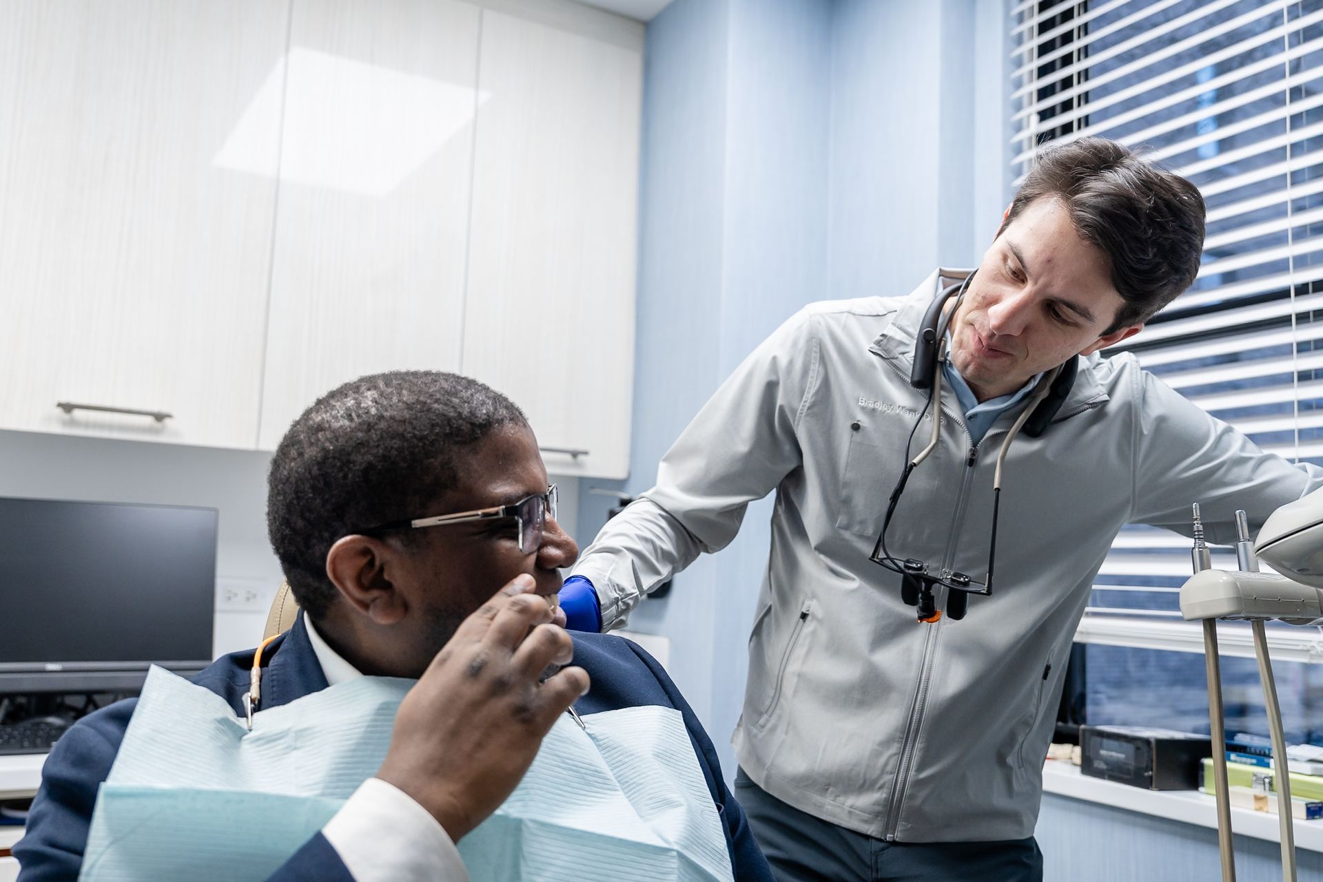 Dentist examines a patient in a dental clinic while speaking with him.