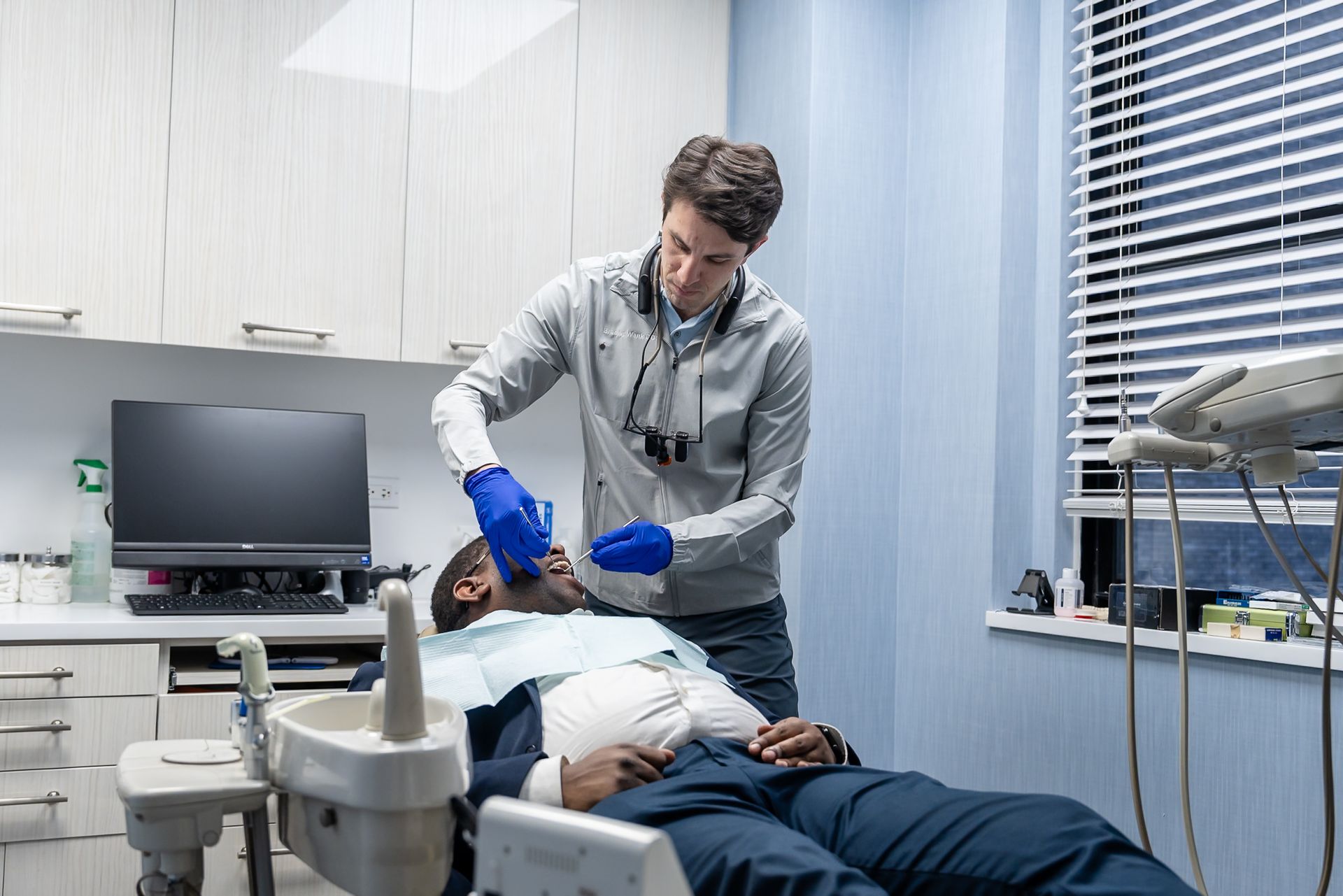 Dentist in blue gloves examining a patient in a dental clinic room.