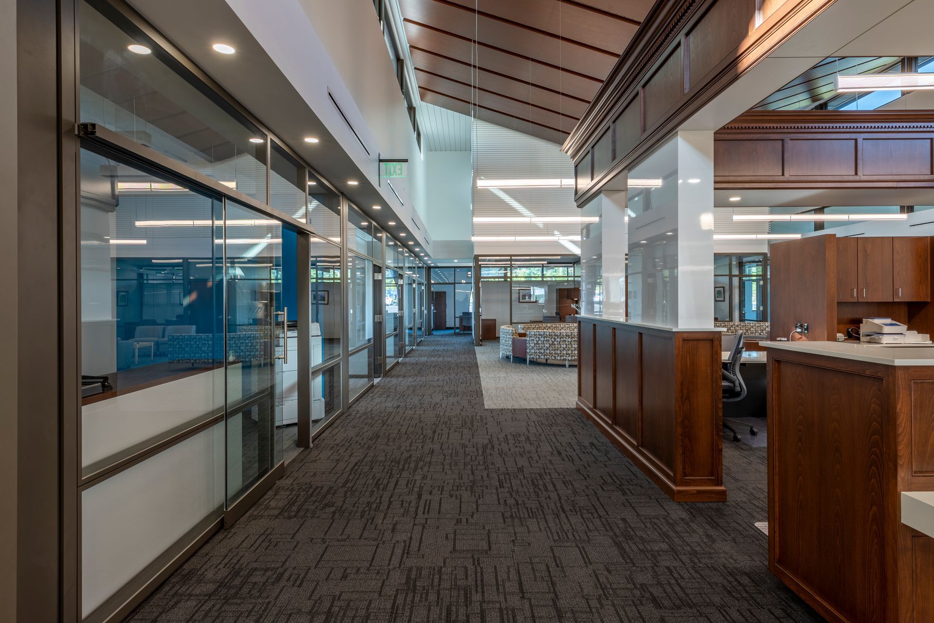 A long hallway in a building with a lot of windows and a reception desk.