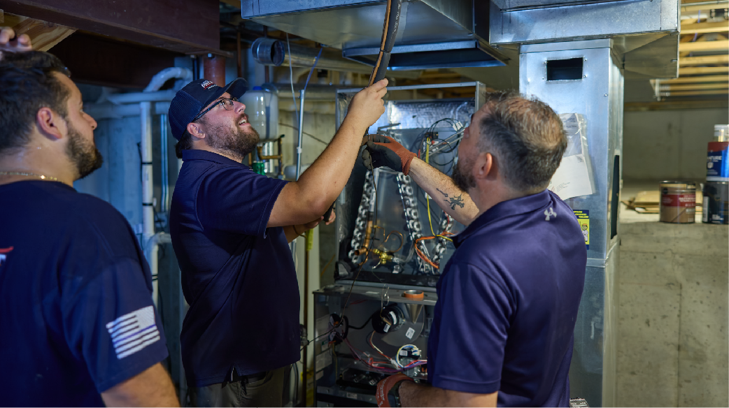 Three workers in blue shirts inspecting machinery in an industrial room
