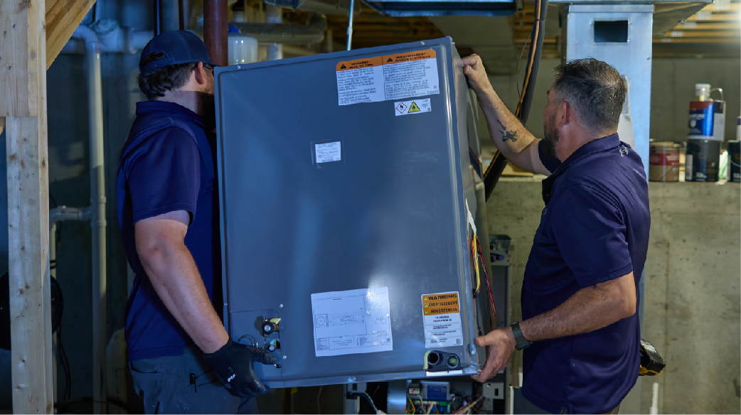 Two workers in dark shirts moving a large appliance in a warehouse setting