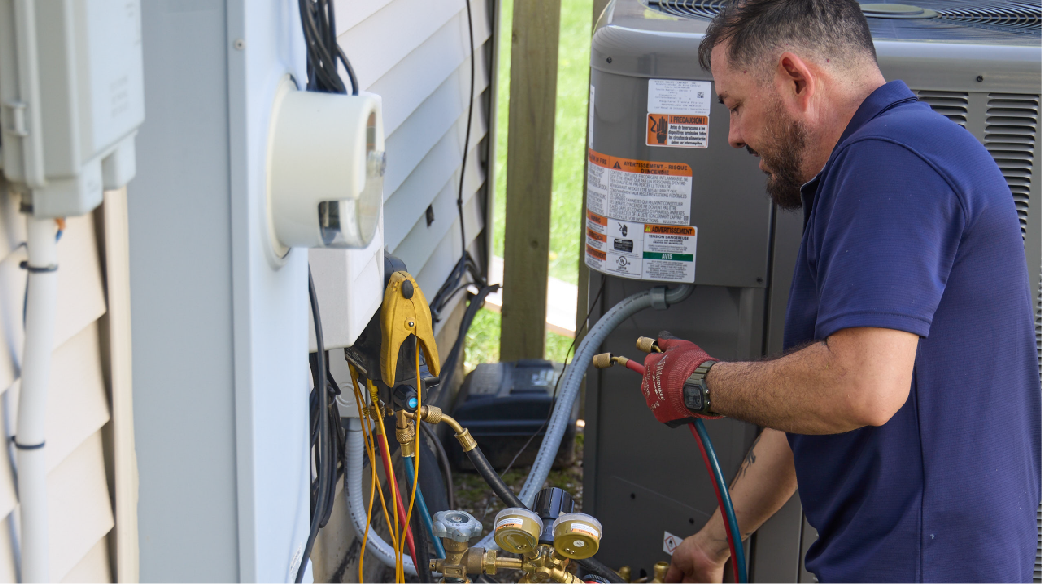 Technician in a blue shirt servicing outdoor HVAC equipment with tools and gauges