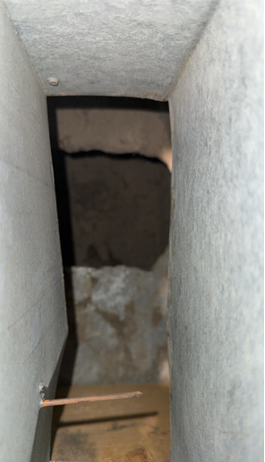 Narrow vertical shaft with dark opening, rough walls, and a wooden plank at the bottom