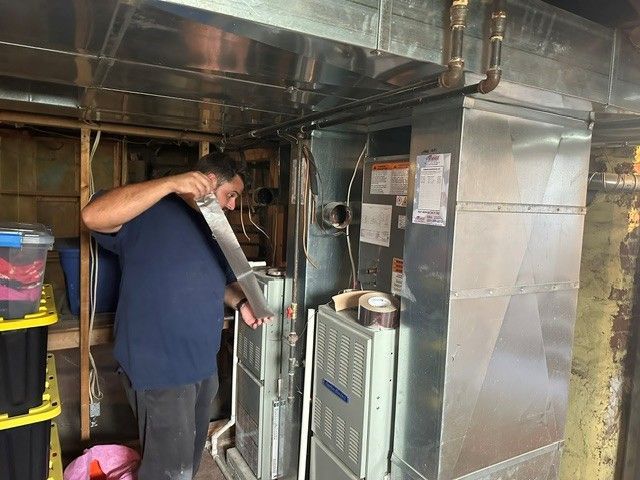 Technician inspecting HVAC equipment in a tight industrial utility room with exposed ductwork.