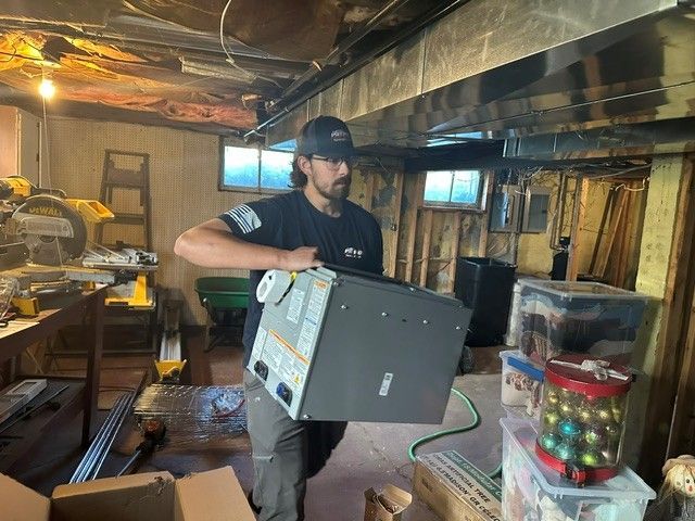 Worker carrying a gray appliance through a cluttered basement workshop