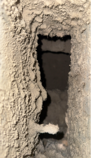 A narrow vertical opening in a rough beige wall, with a dark interior behind it.