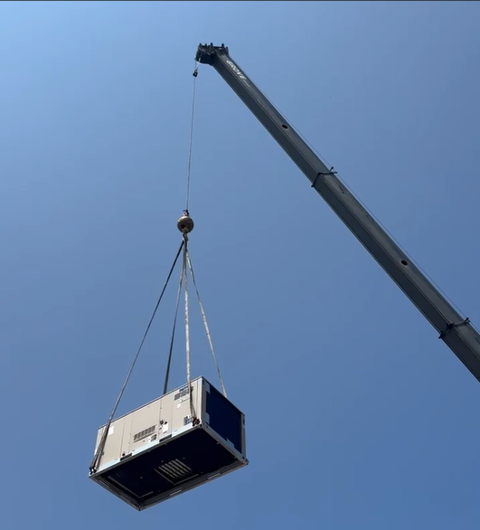 Crane lifting a large white-and-blue HVAC unit against a clear blue sky