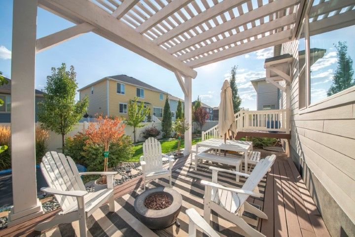 Covered wooden deck with white chairs and fire pit overlooking a backyard and neighboring houses