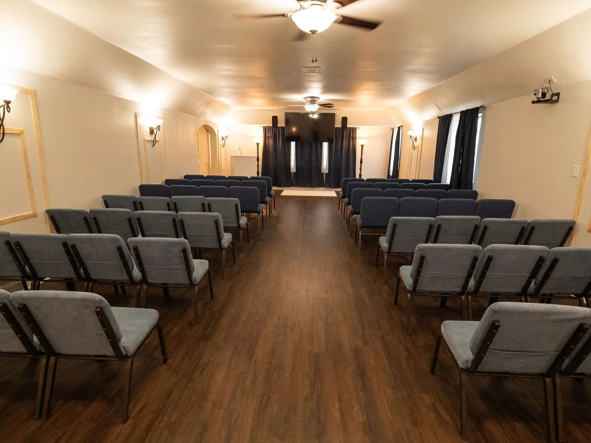 A long hallway filled with rows of chairs and a ceiling fan.