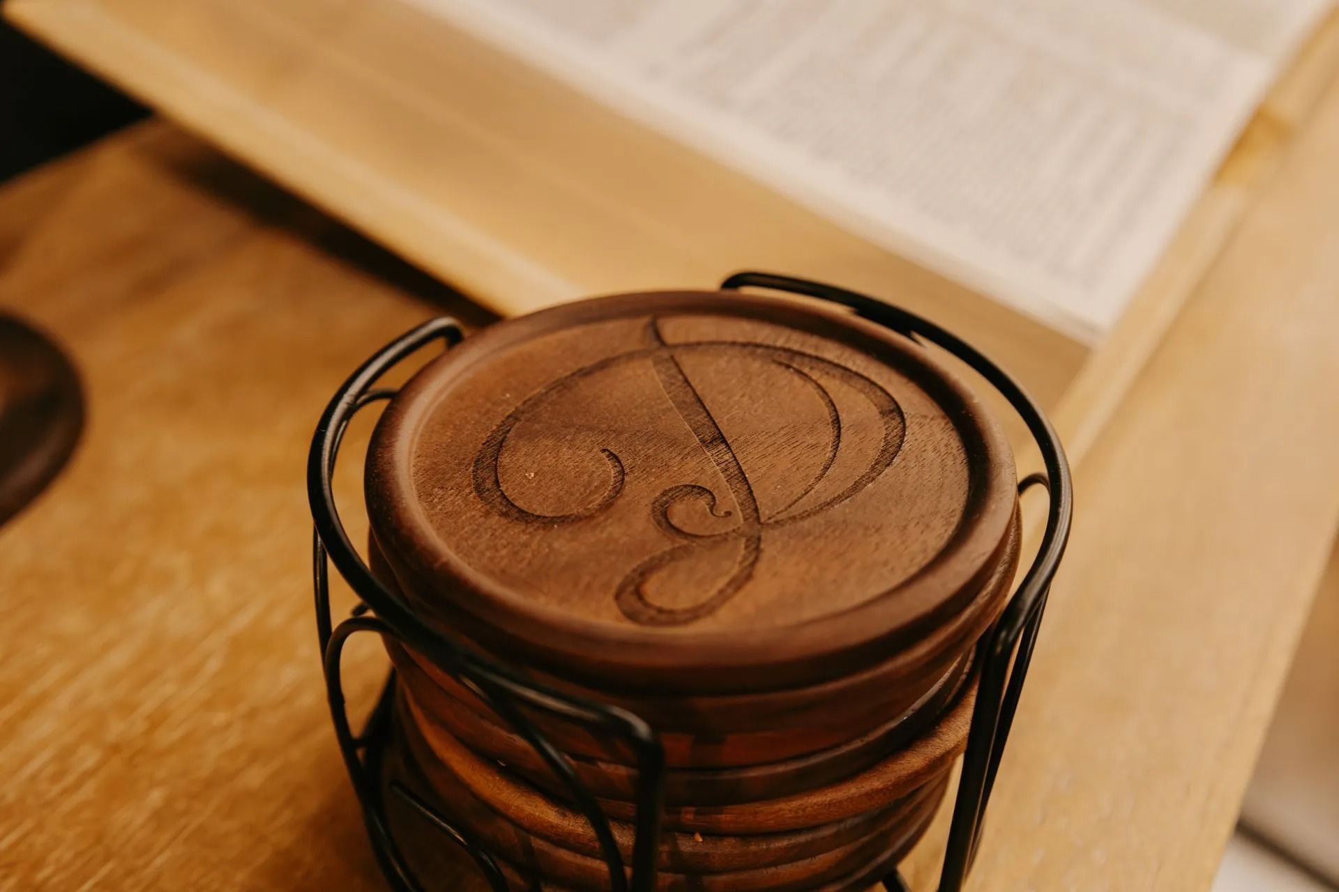 A stack of wooden coasters with a monogram on them are sitting on a wooden table.