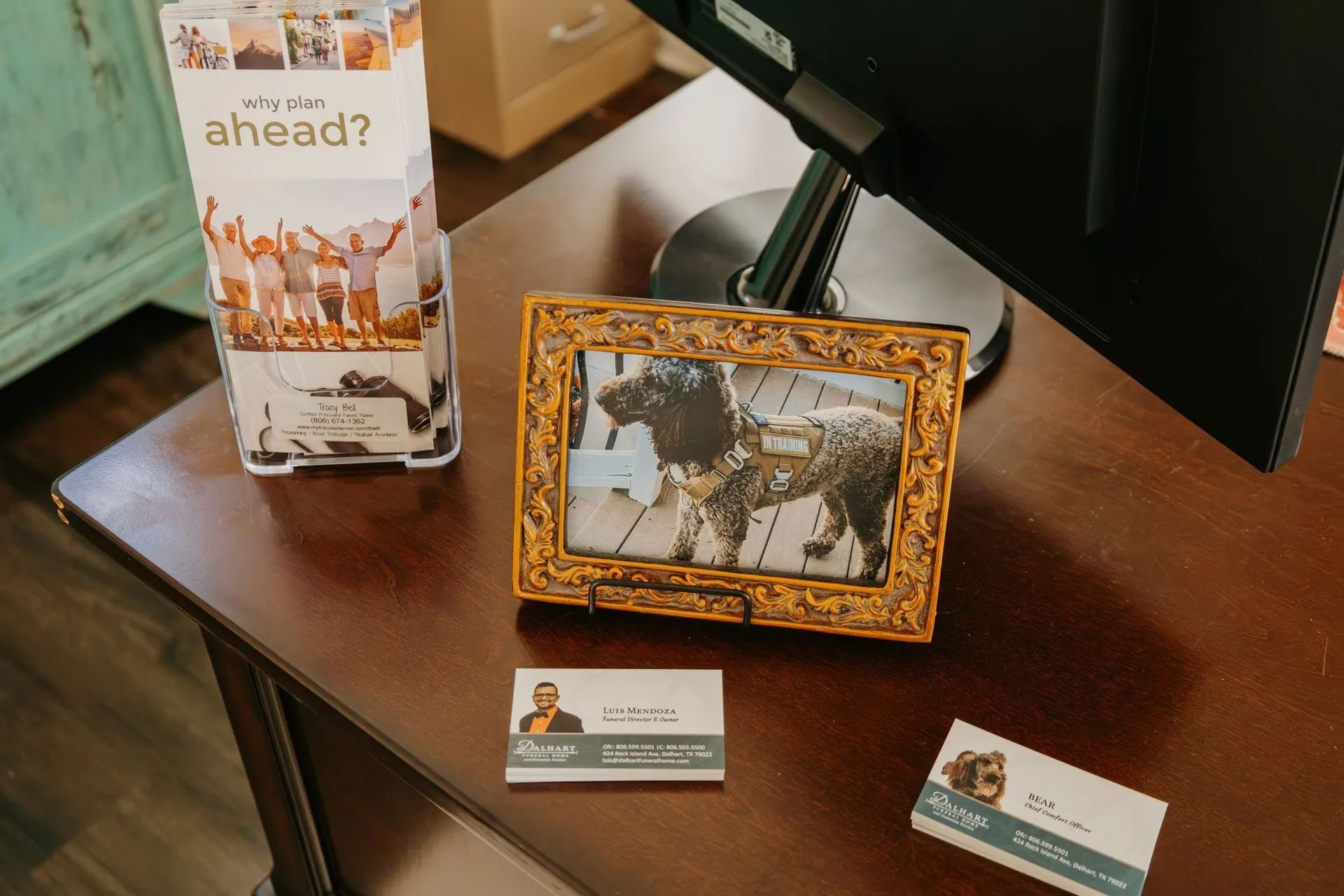 A picture of a dog in a frame is sitting on a desk next to a computer.