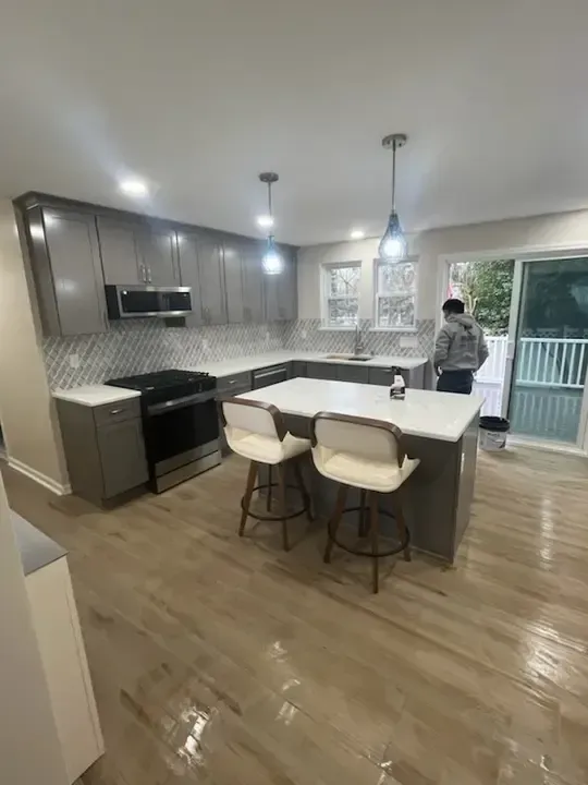 Modern kitchen with white island, gray cabinets, and a person by the sliding door
