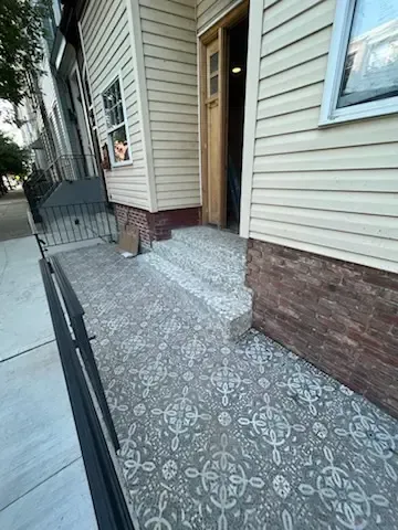 Front porch with patterned tile floor, brick-and-siding wall, and open doorway on a residential building.