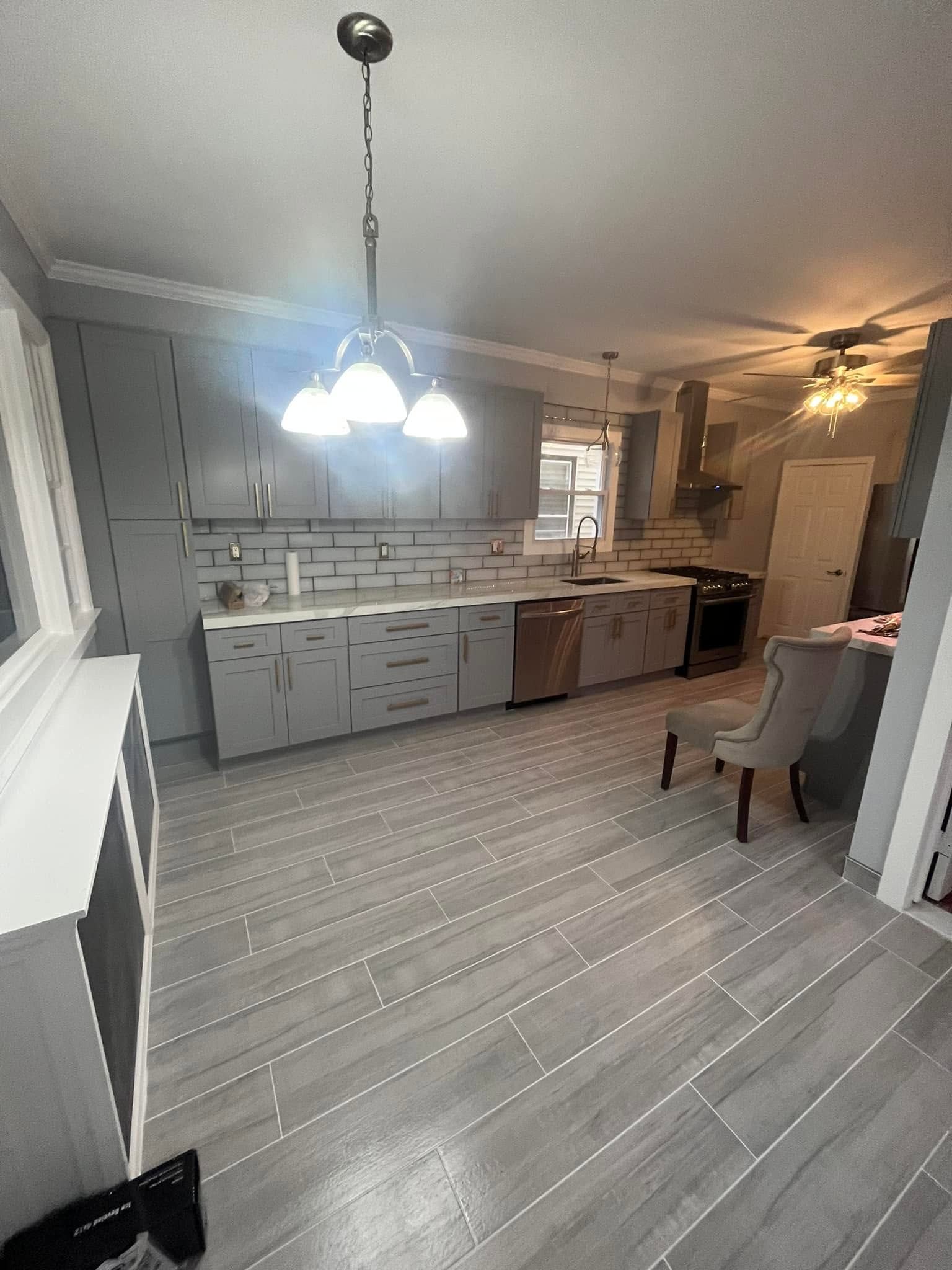 Open kitchen with gray cabinets, striped floor, white island, hanging pendant light, and a chair by the counter