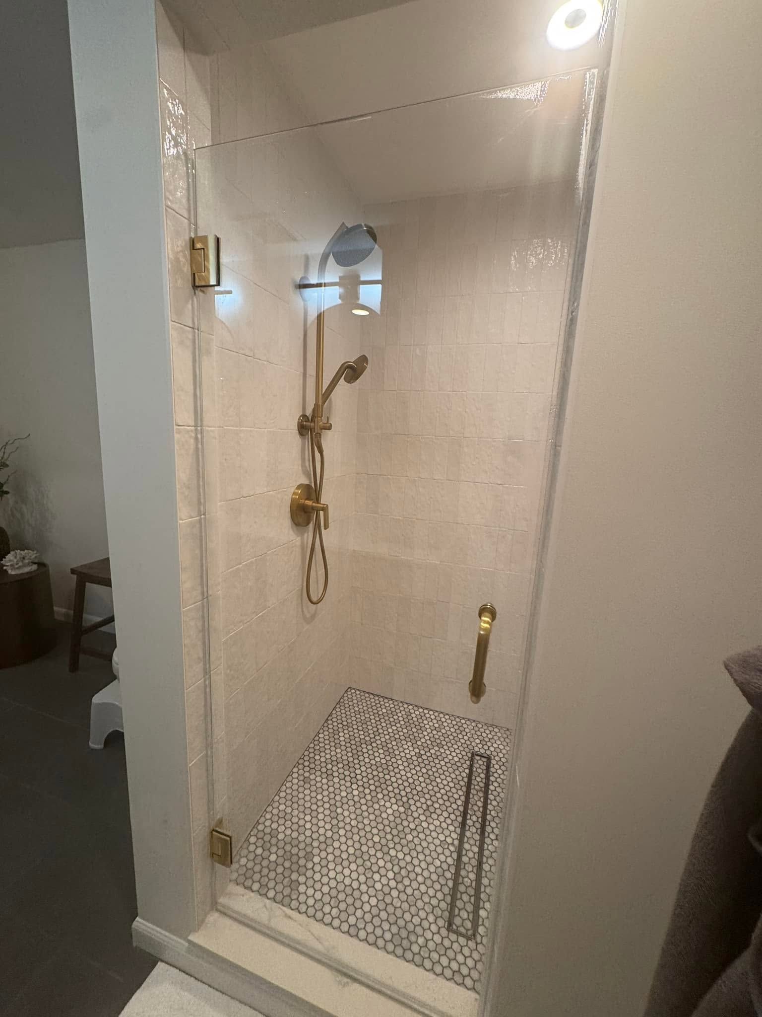 Tiled walk-in shower with brass fixtures, handheld showerhead, built-in bench, and mosaic floor tiles
