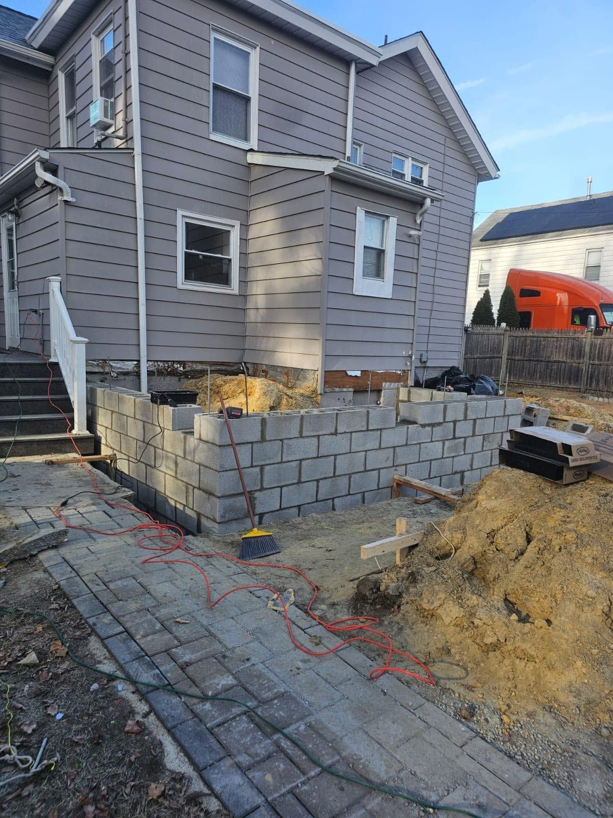 House exterior with a partially built cinder block retaining wall and dirt mound in front