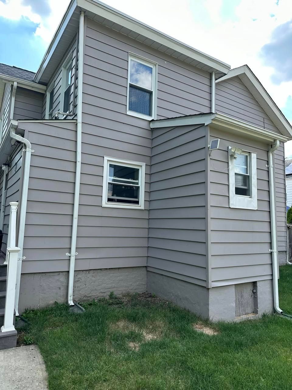 Side of a gray house with white trim, windows, and a small grass yard.