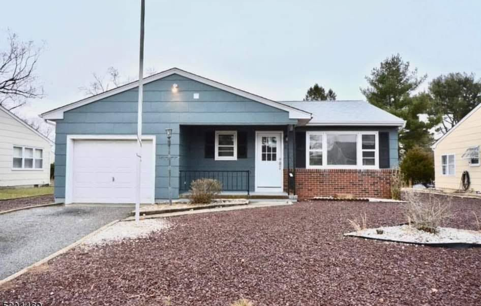 Single-story blue house with white trim, garage, and a rock-covered front yard