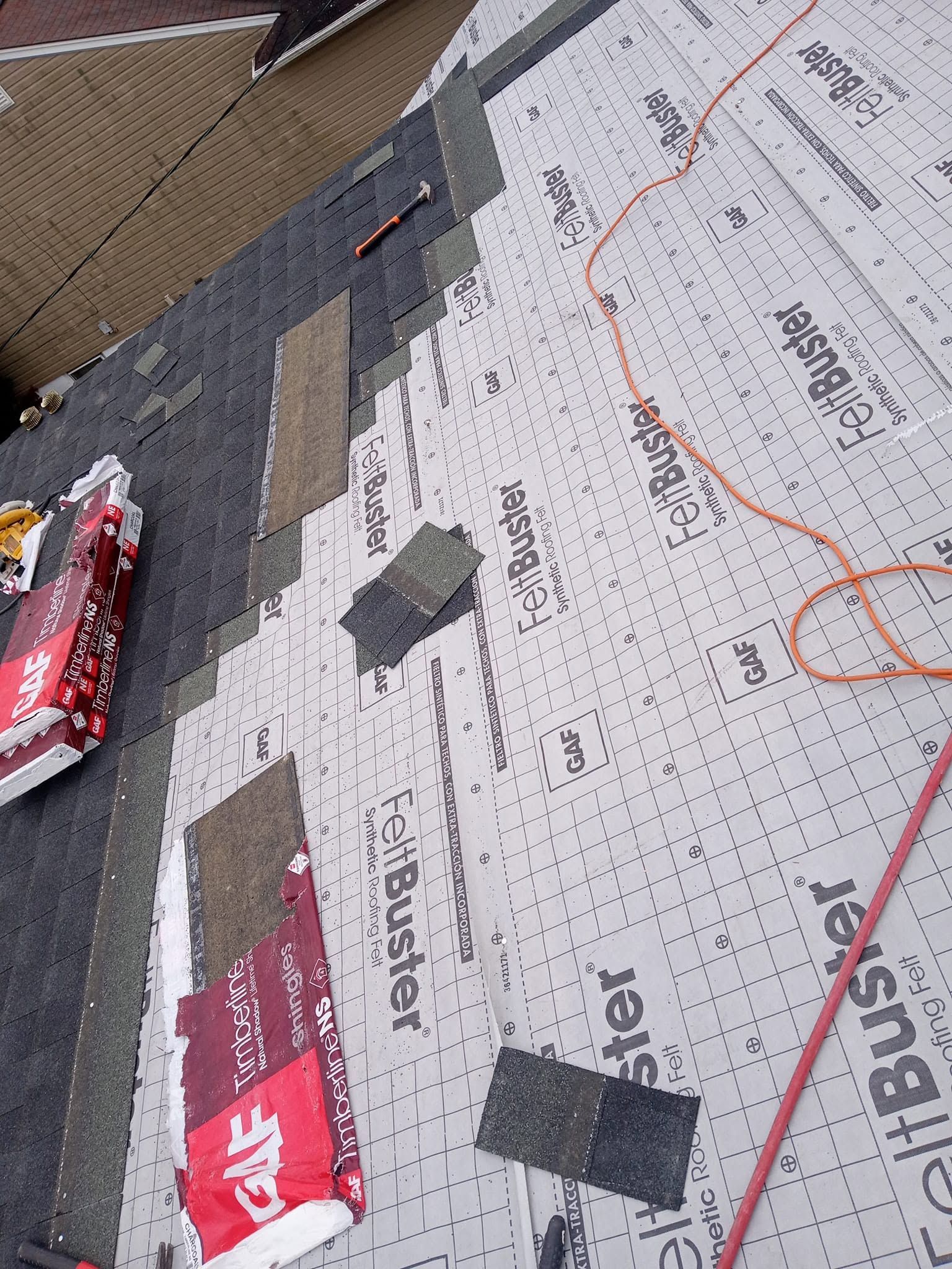 Roofing materials and black tape on a gray roof underlayment, with orange cord and red packaging visible.