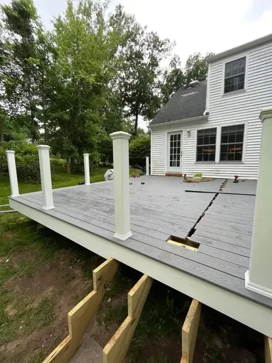 Partially built gray deck with white rail posts beside a white house