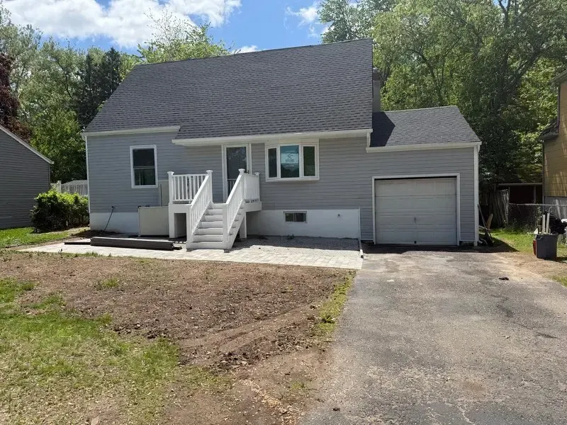 Gray house with front steps, single-car garage, and driveway under a sunny sky