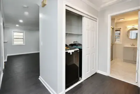 Modern hallway with dark flooring, white walls, and an open closet beside a bathroom entry