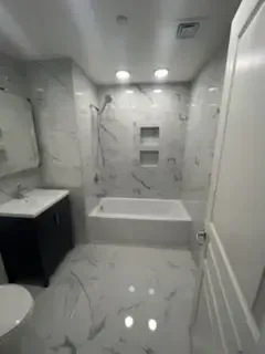 Small white bathroom with tub, shower, sink, toilet, and glossy marble-pattern floor and walls