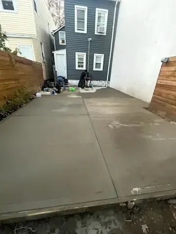 Concrete driveway beside narrow houses with a person near the back wall and scattered items.