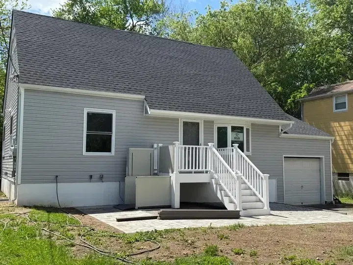 Gray house with white deck and stairs leading to the back door, attached garage on the right.