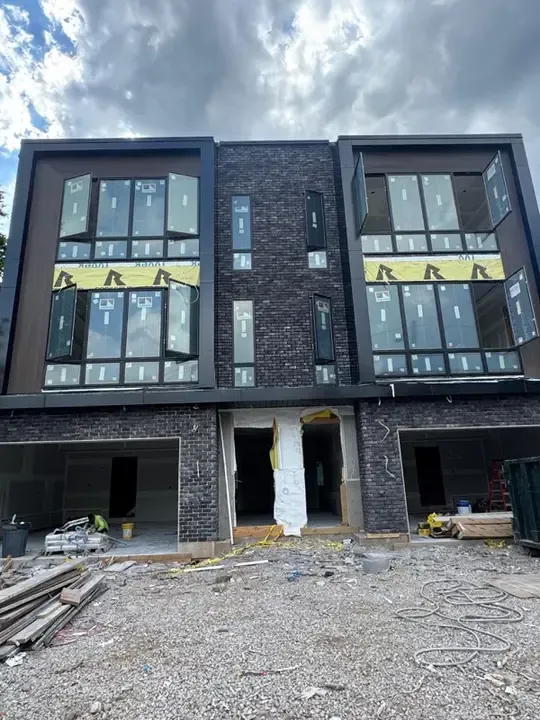 Three-story modern brick townhouse under construction with exposed gravel foreground and unfinished ground level