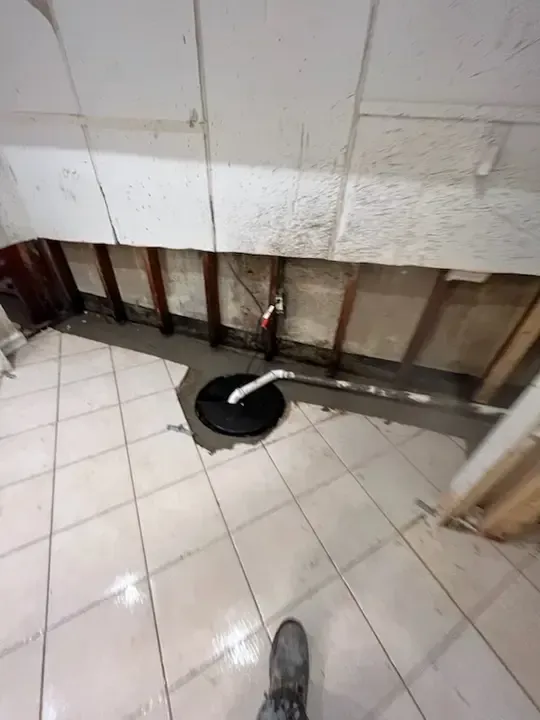 Bathroom floor with exposed wall plumbing, a black toilet base, and white tile flooring.