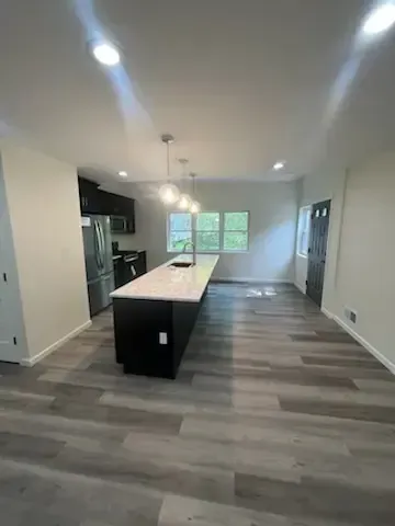 Modern kitchen with a large island, stainless fridge, white walls, and gray wood-look flooring.