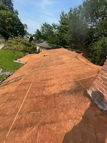 Rusted orange roof on a house surrounded by green trees and lawn, viewed from above