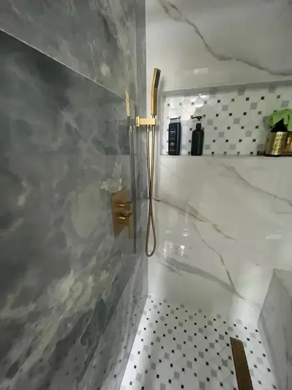 Modern bathroom shower with gray and white marble tile, glass door, and gold fixtures