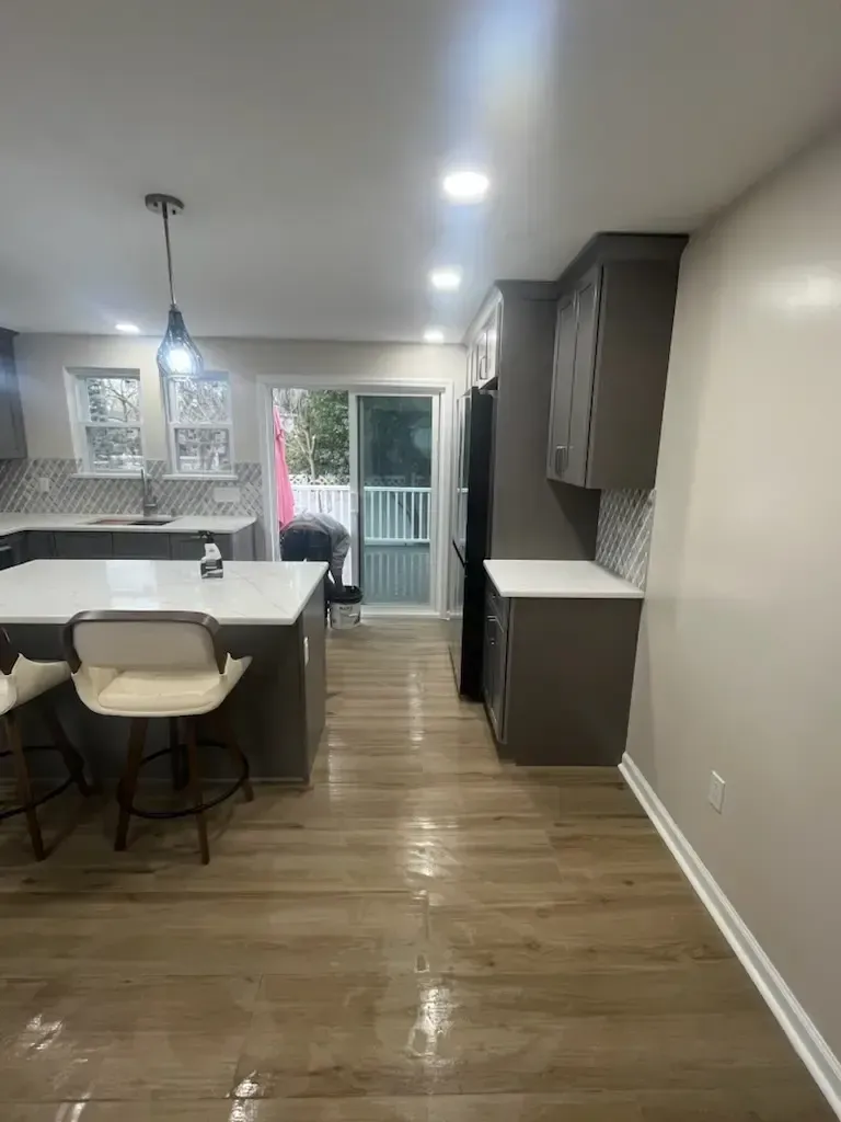 Modern kitchen and dining area with island, pendant light, wood floors, and sliding glass door to patio.