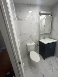 Small bathroom with marble-pattern walls, toilet, and black vanity with mirror.