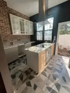 Bright modern kitchen with brick wall, white cabinets, island, and geometric floor tiles.
