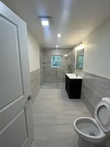 Modern white bathroom with toilet, vanity, and tiled walls, viewed from the doorway