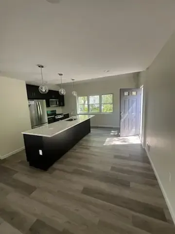 Empty modern kitchen with black island, light wood floors, and sunlight through the window.
