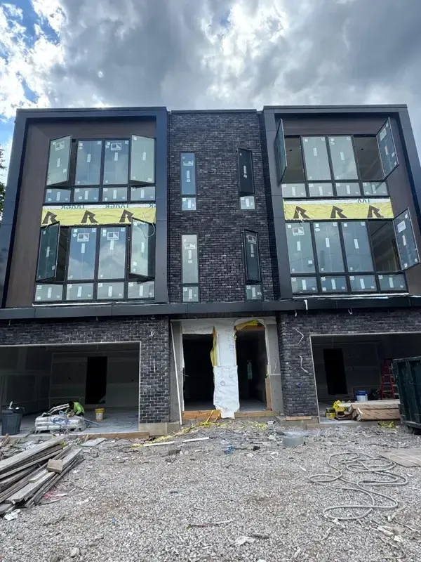 Front view of a new three-story townhouse building with dark brick and unfinished entryways