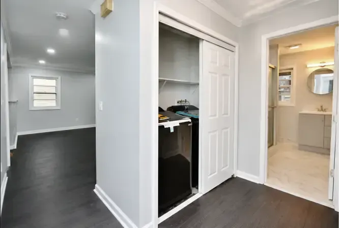 Bright entry hallway with dark wood floors, white walls, closet, and a view into a beige bathroom.