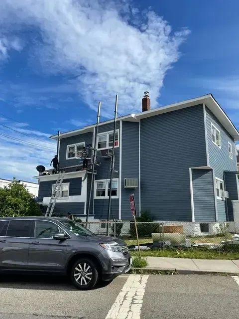 Blue two-story house with white trim and a parked dark SUV under a partly cloudy sky