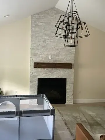 Living room with stone fireplace, hanging black light fixture, and playpen in the foreground