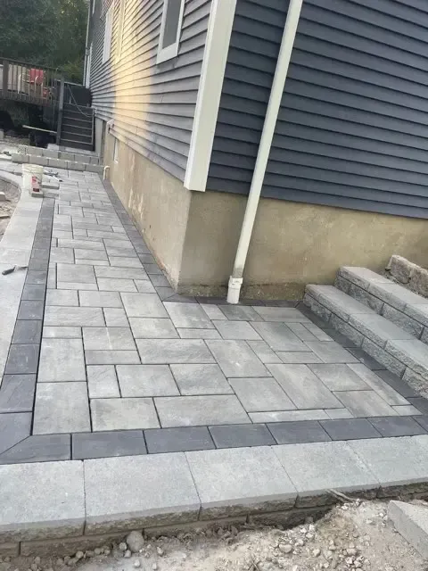 Fresh gray paver walkway beside a house with concrete steps and a downspout