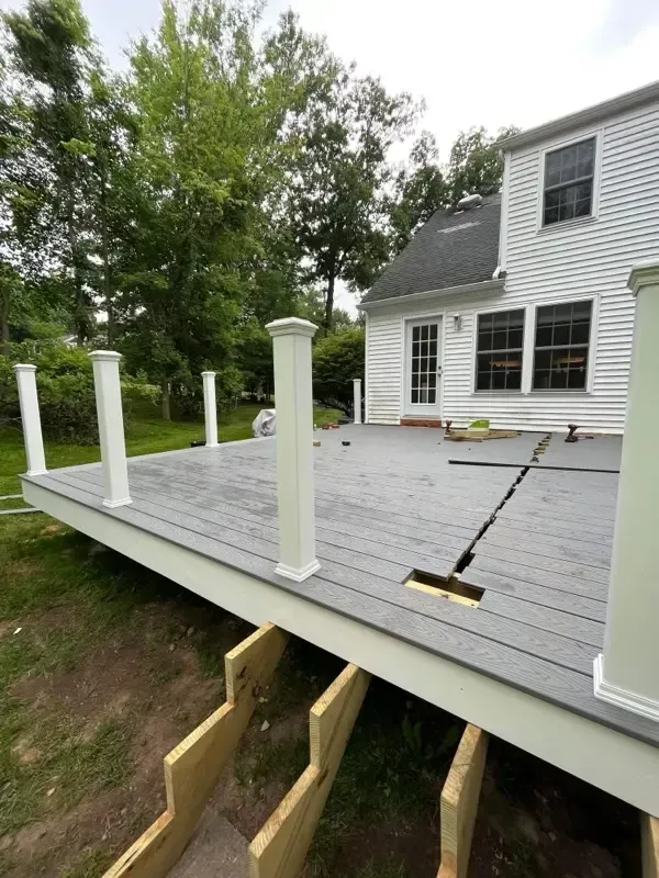 Partially built gray deck beside a house with white posts and exposed framing underneath