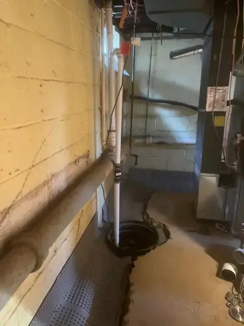Basement utility area with pipes, furnace equipment, and a yellow brick wall.