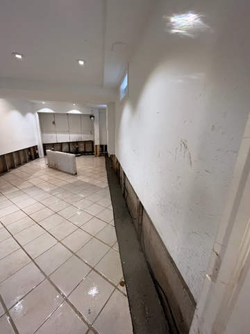 Curved white-tiled hallway with scuffed walls, recessed lights, and a low barrier in the center.