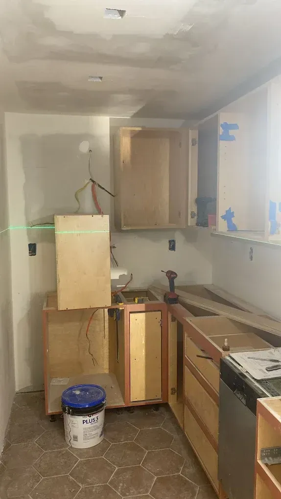 Narrow kitchen under renovation with unfinished cabinets, tools, and a bucket on the floor